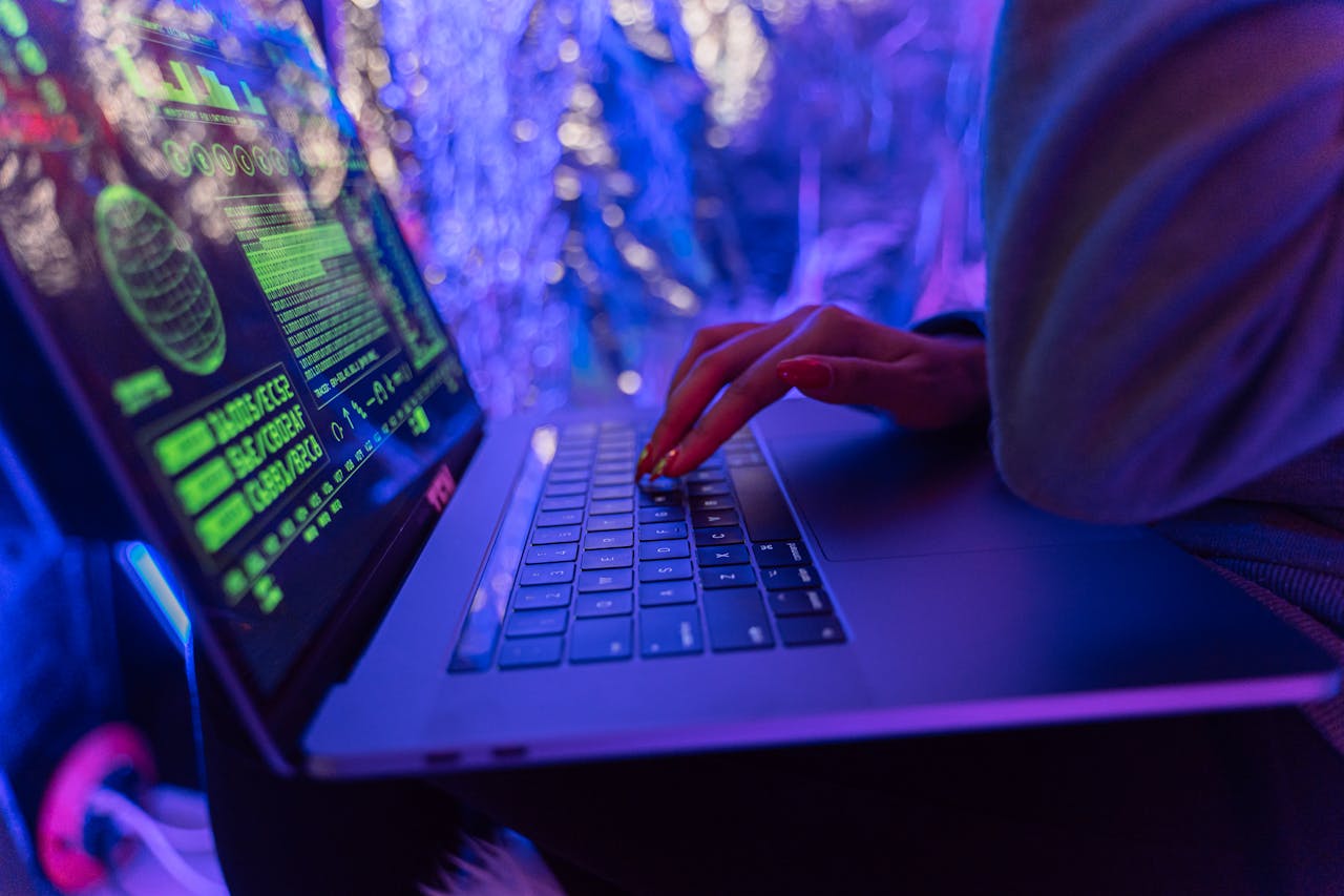 Close-up of hands typing on a laptop displaying cybersecurity graphics, illuminated by purple light.